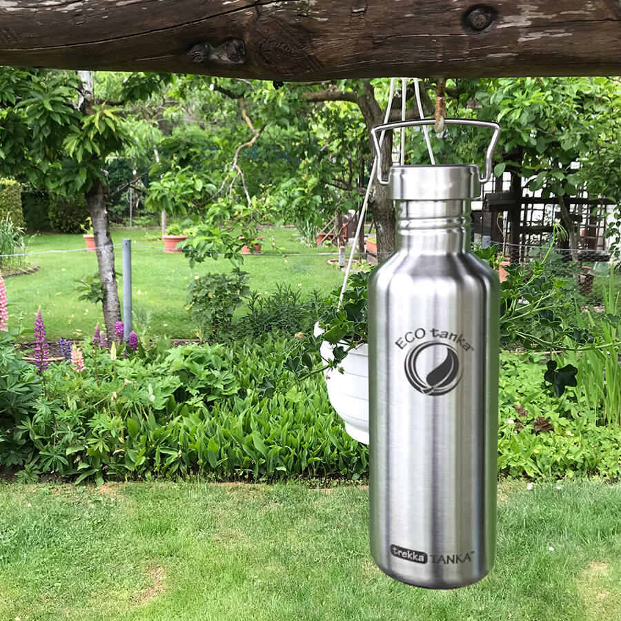 trekkaTANKA 1,0l mit Wave Verschuss aufgehangen an dem Tragebügel an einem Baum vor einem Gartenhintergrund